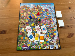 Wide shot of the board of candy land with the tactile clear overlay on it. The 3d printed replacement pawns are on the board along with 6 of the cards with braille on them.