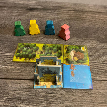 Load image into Gallery viewer, The meeples with braille on them. in front of them is the starting castle, and two domino tiles with forest and water. All are labeled in braille
