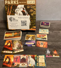 Load image into Gallery viewer, The parks game box with a bunch of types of cards and tokens set out that have been modified with transparent braille
