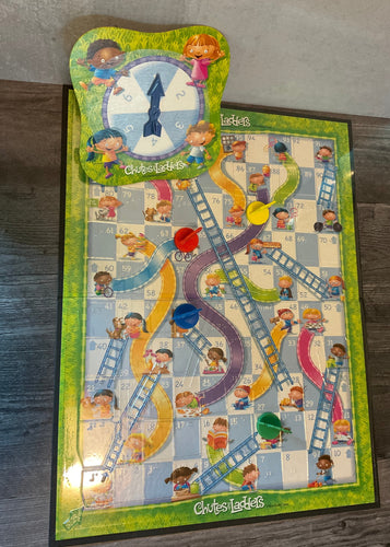 The chutes and ladders board. The spinner can be seen at the top with braille on it, a thermoformed clear board overlay with tactile ladders and chutes. The 3d printed pieces are also seen