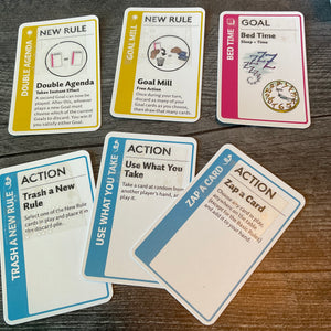 A close up on some rule cards, a goal card and some action cards. The action cards have their function embossed on them in braille.