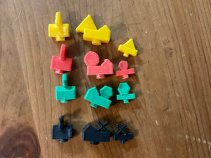 All the types of player pieces. Each color has a distinct shape on them, red circles, black xs, yellow triangles and green hexagons