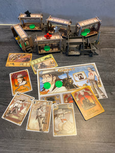 A shot showing the train cars. On the train car you can see the player pieces and the loot. In the foreground you can see the cards and a player mat. All of the pieces and cards have braille on them.