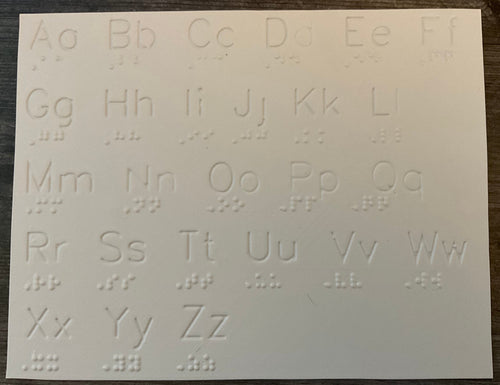 The white plastic sheet has print and braille letters. The print letters are extruded down.