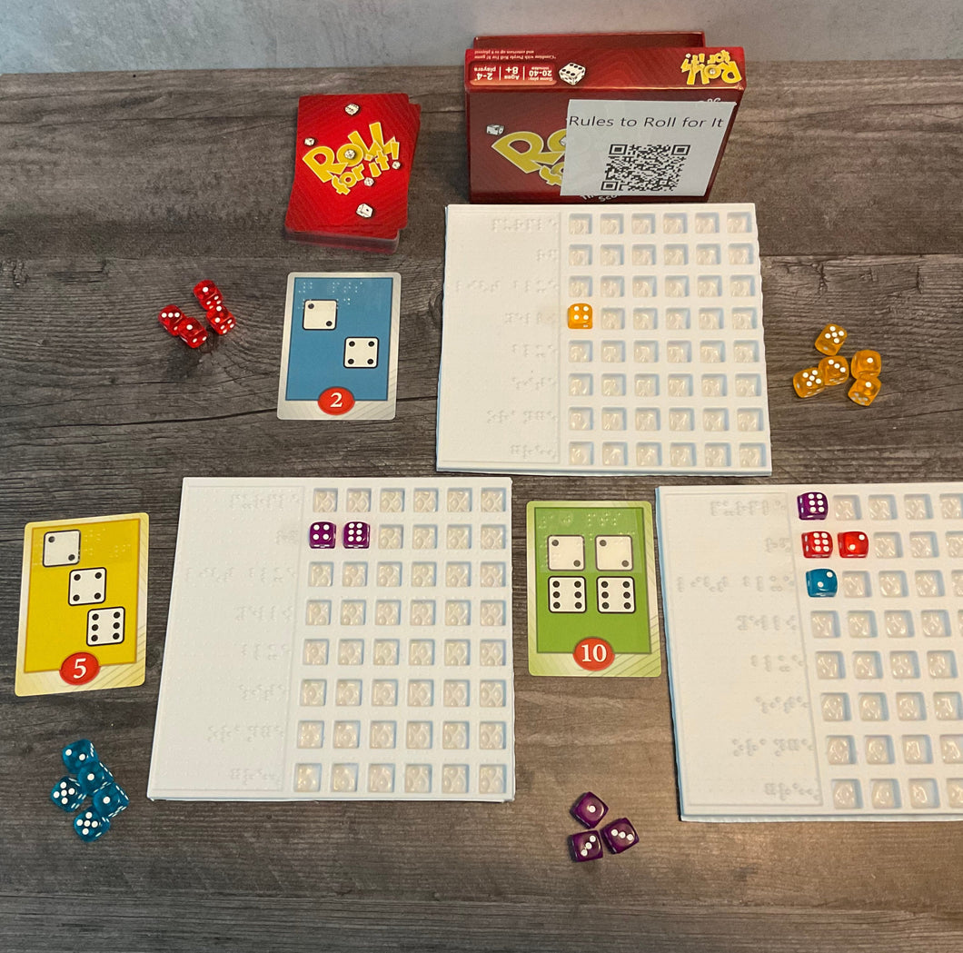 The game is shown setup(red version). There are trays next to the cards to sort who's dice are who's. The cards all have transparent braille on them indicated the needed dice and their point value
