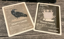 Load image into Gallery viewer, A close up of the crafty crow and trash panda cards. Both have transparent braille on them
