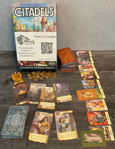 The box of Citadels along with all the different types of cards. Cards have the gameplay information on them in transparent braille.