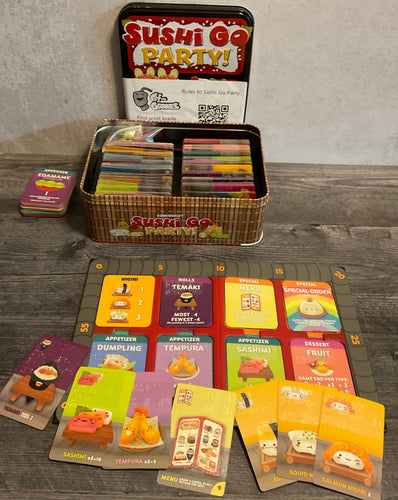 The sushi go party game and board. Cards are laid out in front of the board. Both the board and the cards have transparent braille on them