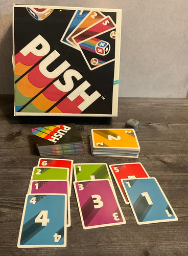 The game push. The cards with their numbers and colors are arranged in rows as one would do in the game. The 3d printed die can be seen in the background