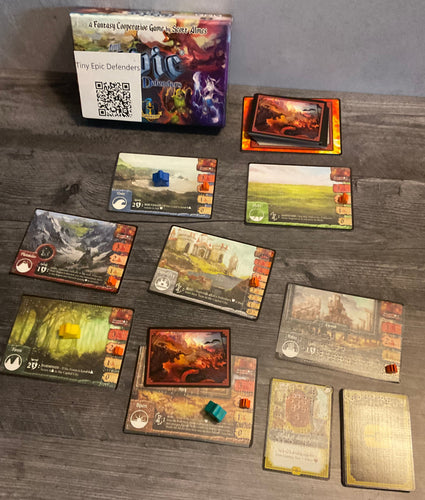 The different locations set up. each has transparent braille on both sides and a damage indicator on them. Artifact cards can be seen in the foreground with transparent braille on them