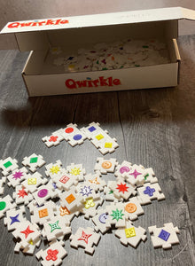 Picture of the braille box with the Qwirkle pieces shown on the table. Tactile braille and shapes are on all the interconnecting pieces.