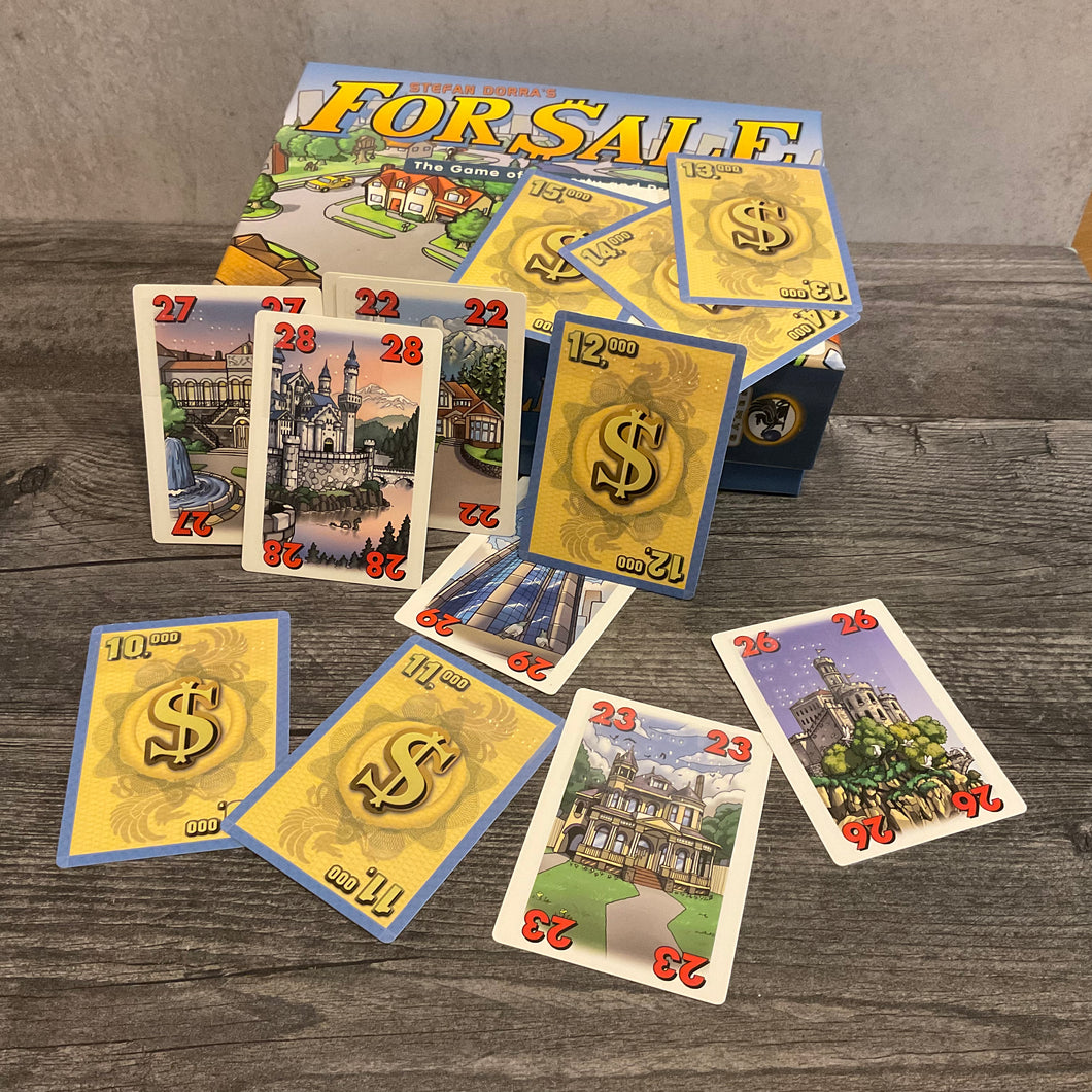 For Sale box with face up cards with houses and numbers on them as well as cards with money showing. All cards have braille stickers on them.